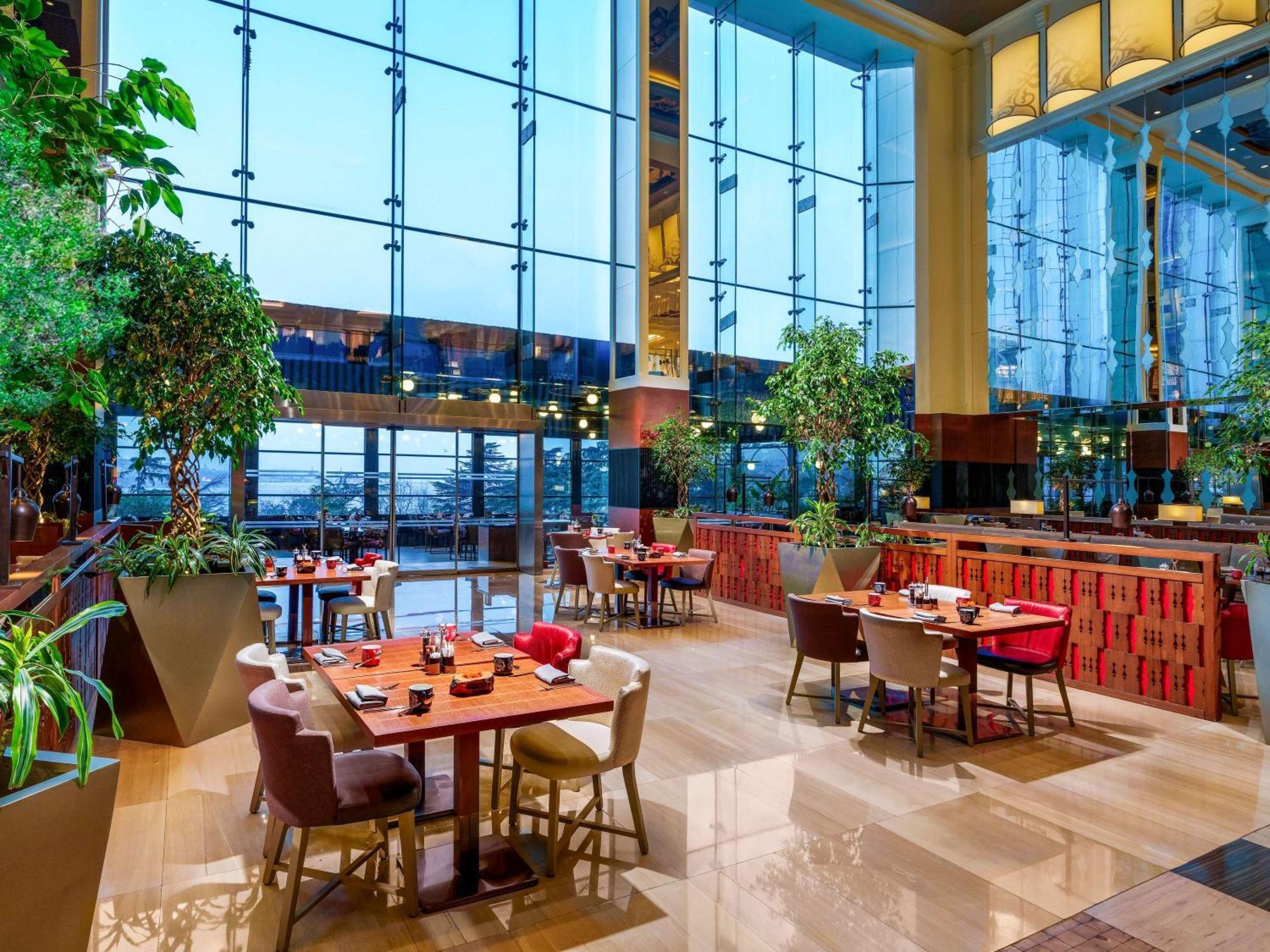 Swissotel The Bosphorus Istanboel Buitenkant foto The photo shows a modern restaurant interior featuring large glass windows that allow plenty of natural light to enter. The decor includes lush greenery, with potted plants placed throughout the space. There are several dining tables arranged comfort