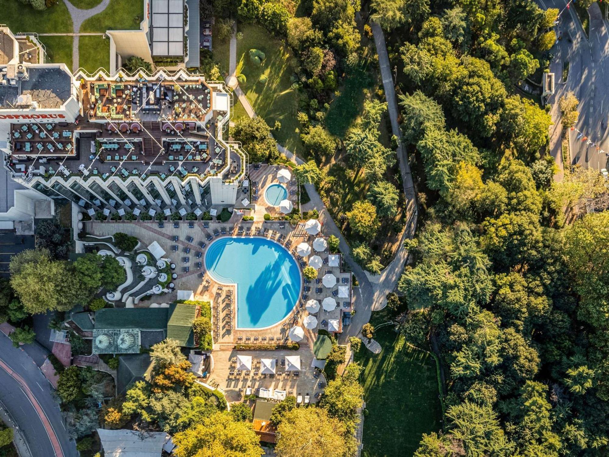 Swissotel The Bosphorus Istanboel Buitenkant foto The photo shows an aerial view of a hotel complex surrounded by lush greenery. In the center, there is a large, blue swimming pool, with several lounge chairs arranged around it. The hotel building has a modern architectural design, featuring multipl