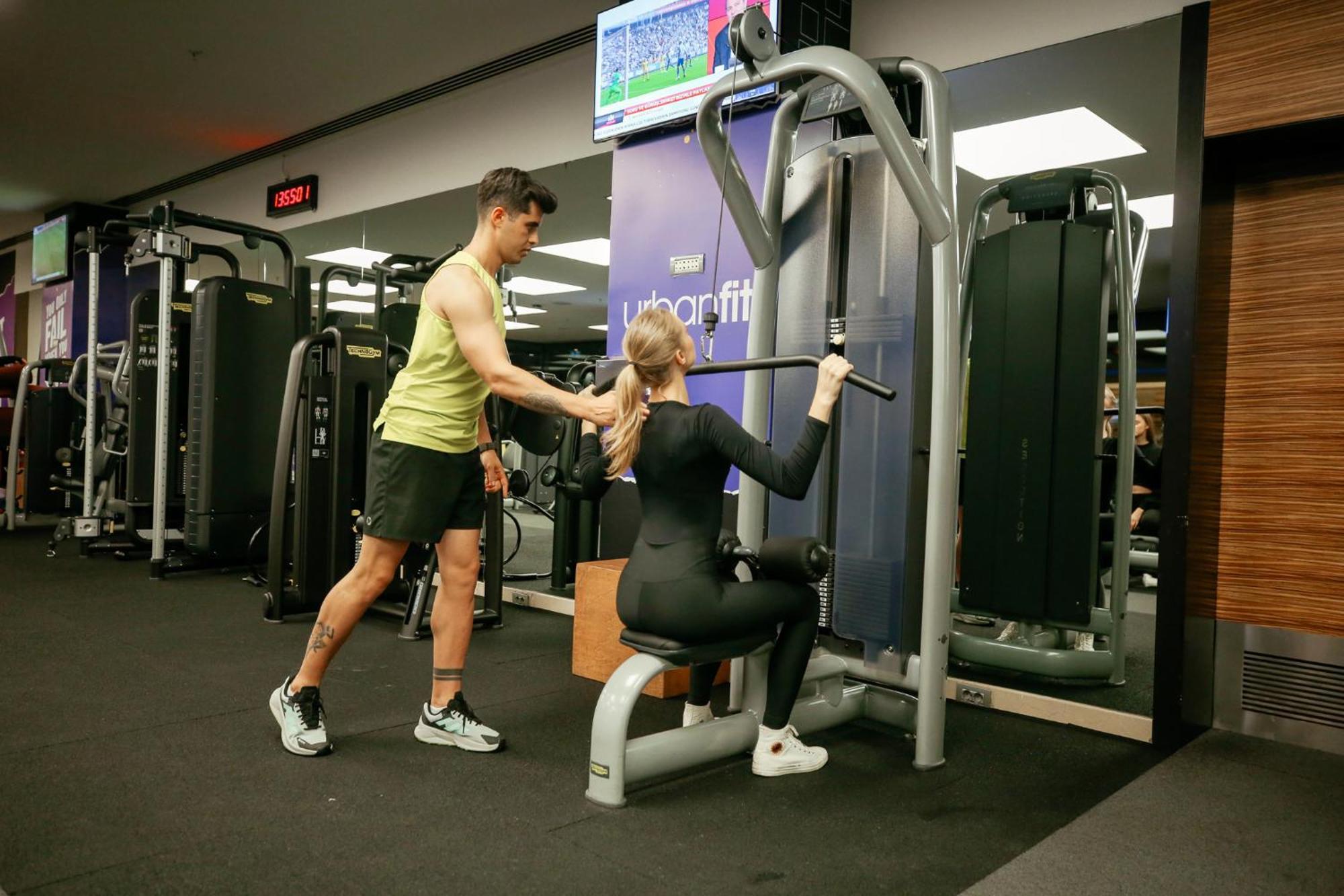 Swissotel The Bosphorus Istanboel Buitenkant foto The photo shows a gym scene where a man is assisting a woman with her workout. The woman is seated on a weight machine, performing a rowing exercise, while the man stands beside her, likely providing support or guidance. In the background, there is a